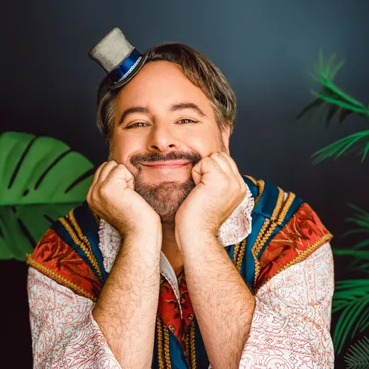 A comedian of Ménage à Moi rests his chin on his hands with a cheeky grin