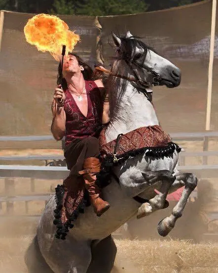 A fire-breather spits a fireball from the back of a rearing grey horse