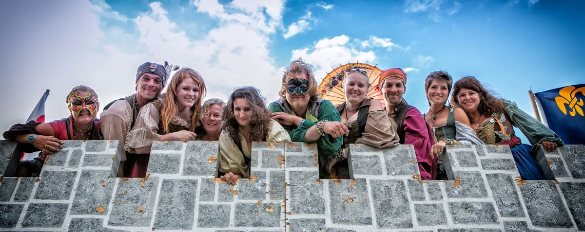 The faire's cast leans over the castle wall, waving to arriving guests